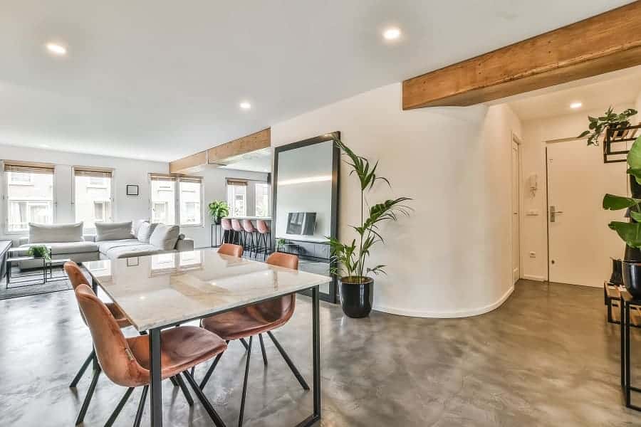 Open woonruimte met een glanzende lavasteen gietvloer, houten balken, een marmeren eettafel, lederen stoelen en kamerplanten.
